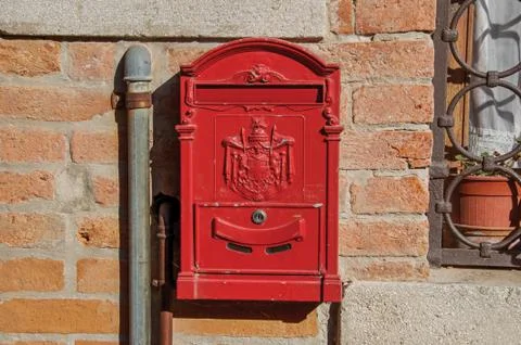 Close-up of a red post box stuck in a brick wall in the sunset at Venice Stock Photos