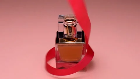 Close-up. The red ribbon wraps around a square bottle of golden perfume Stock-Footage 151294514