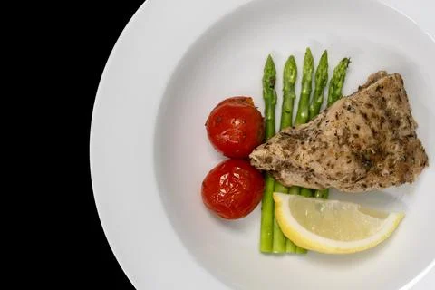 Close-up, Red snapper steak, asparagus, tomatoes, and lemon on a white plat.. Stock Photos