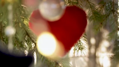 A close-up of a red soft heart toy hanging on a Christmas tree among toys and Stock Footage 296402805