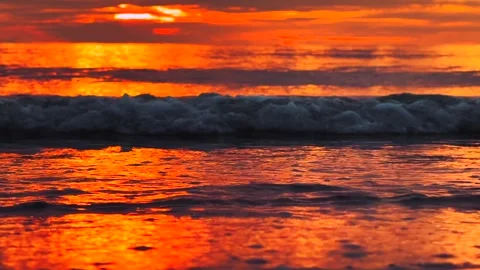 Close up of red sunset with waves rolling onto the shore and glowing reflections Video stock 321289159