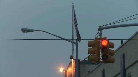 Close up of red traffic light with American flag waving in background, dusk. Video stock 108333044