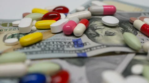 Close up, with red, white, colored pills rotating on dollars banknotes on white Stock Footage 86177726