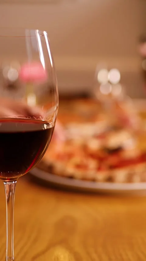 Close Up of Red Wine Glass with Pizza Dinner in Background Stock Footage 337875573