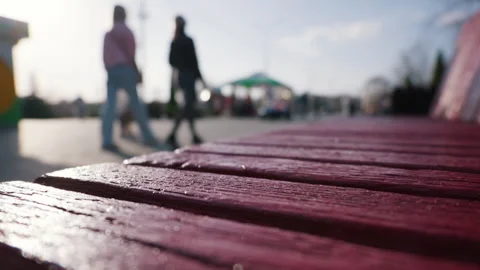 Close up of red wooden bench with blurred silhouettes walking in a spring park. Stock Footage 331860945