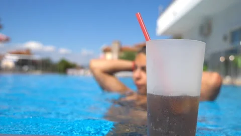 Close up of refreshing cocktail with straw standing near pool. Young girl Stock Footage 311624491