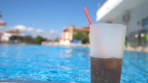 Close up of refreshing drink with straw standing near empty pool of hotel. View 스톡 동영상 331395479