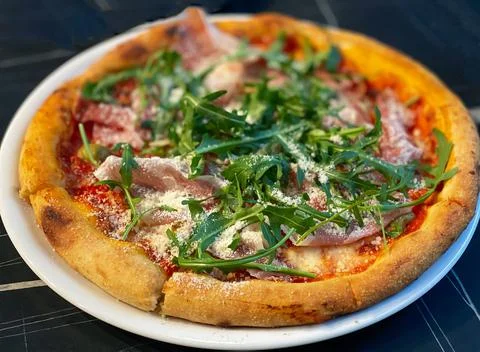 Close-up on a restaurant table pizza with prosciutto, arugula and parmesan Stock Photos