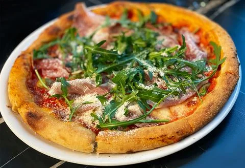 Close-up on a restaurant table pizza with prosciutto, arugula and parmesan Stock Photos