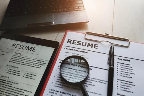 Close-up of resume with magnifying glass, computer laptop and pen on wooden.. Stockfoto's