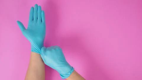 Close up of Right hand is pulling blue latex gloves on pink background. Stock Photos