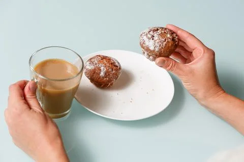 Close up of right hand taking one of two curd muffins from plate, and left .. Stock Photos
