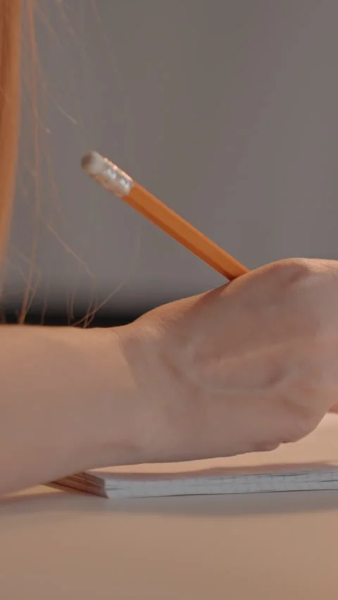 Close up of right hand writing with orange pencil on ruled paper in neutral Stock Footage 345666893