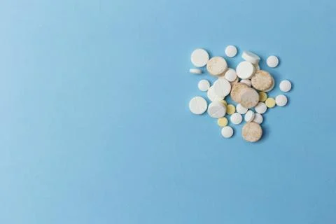 Close up of a right side placed pile of various pills lay on light blue surface 스톡 사진