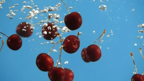 Close up of ripe cherry cherries fall into water blue background. Red berries Stock Footage 91013189