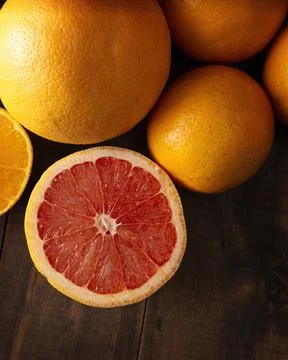 Close up of ripe grapefruit slice and several whole oranges on brown rustic w Stock Photos