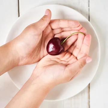A close-up of a ripe large cherry in the shape of a heart in the hands of a girl Stock Photos