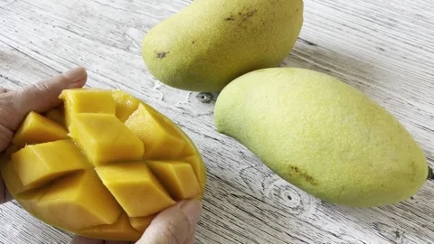 A close-up of a ripe mango. A woman's hands open half of a diced mango. Stock Footage 327250560