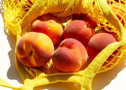 Close-up Ripe peaches in a mesh bag or string bag on light yellow background Stock Photos