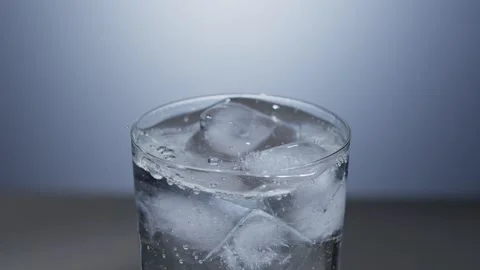 Close-up of ripples caused by an ice cube falling into a glass of water Stock Footage 342727816