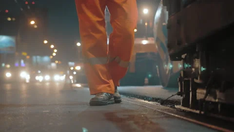 A close-up of a road worker walks next to an asphalt paver. Road repair in the Stock Footage 154967660