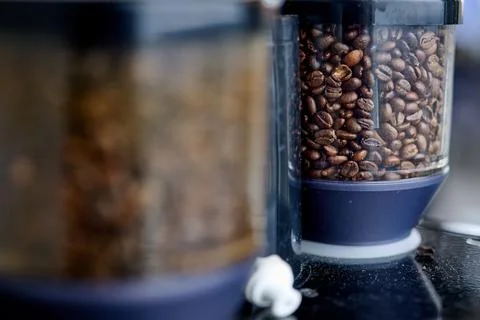 Close up of roasted coffee beans inside a clear plastic grinder hopper of a p Stock Photos
