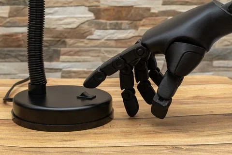 Close-up of robotic or Prosthesis hand interacting with modern lamp on wood.. Stock Photos