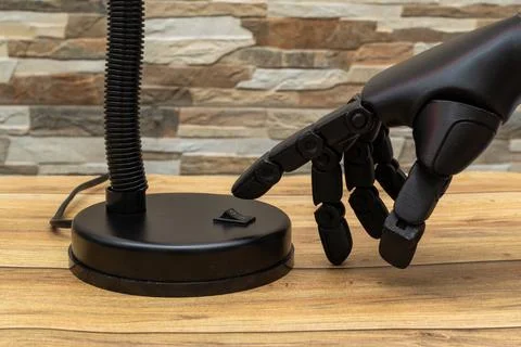 Close-up of robotic or Prosthesis hand interacting with modern lamp on wood.. Stock Photos