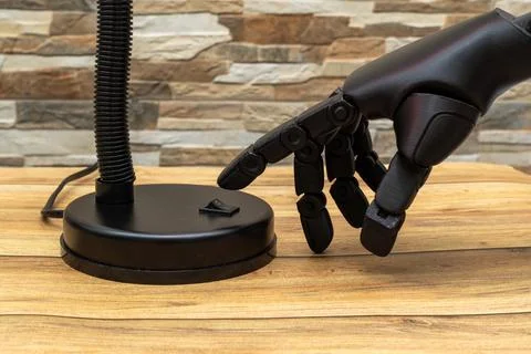 Close-up of robotic or Prosthesis hand interacting with modern lamp on wood.. Stock Photos