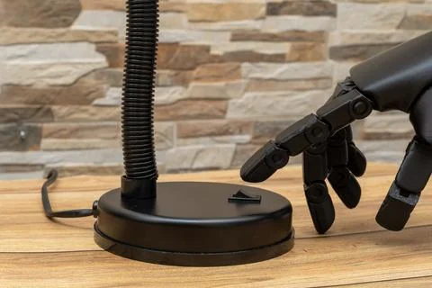 Close-up of robotic or Prosthesis hand interacting with modern lamp on wood.. Stock Photos