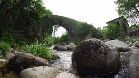 Close up of rock in river with stone bridge during day time, Portugal Stock Footage 128963544