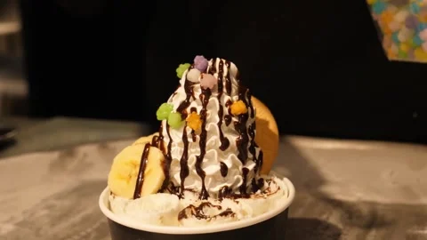 Close-Up of Rolled Ice Cream Sundae with Whipped Cream, Banana, and Chocolate Sy Stock Footage 345293249