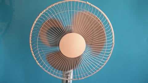 Close-up of a rotating electric fan with blades creating airflow against a blue Stock Footage 340267080