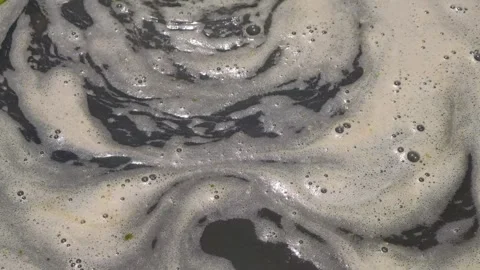 Close-up of rotating foam and bubbles on dark polluted water Video stock 347926615