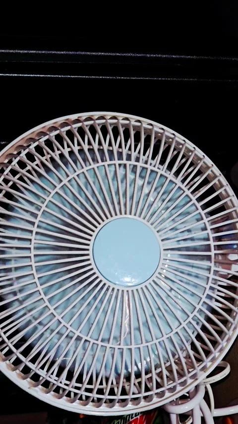 Close-up of a rotating white and blue desk fan on a dark background Stock-Footage 339634888