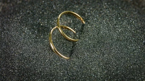 Close up rotation of golden wedding rings on the black sand. Video stock 59792349