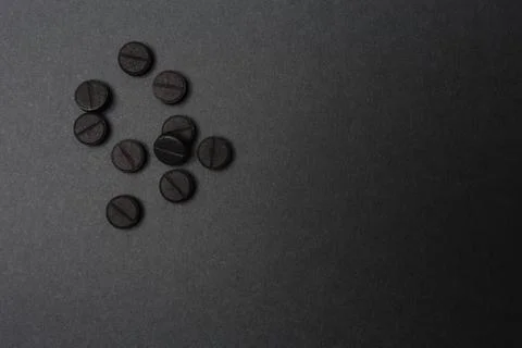 Close up of rough black round tablets in a light spot of dark grey surface 스톡 사진