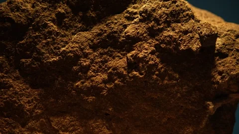 Close-up of rough orange stone against blue backdrop under harsh light Stock Footage 313180343