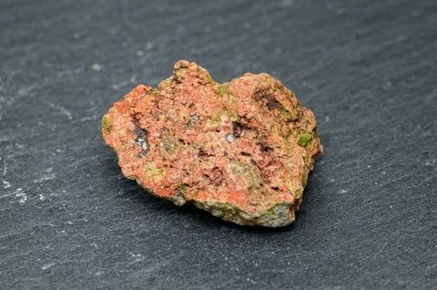 Close-up of a rough, textured, reddish-orange mineral specimen with green m.. Фото