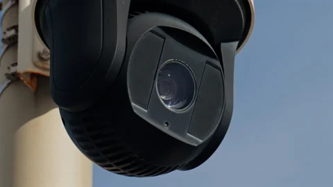 Close up of a round, black surveillance camera mounted on a white pole with the Stock Footage 308697530