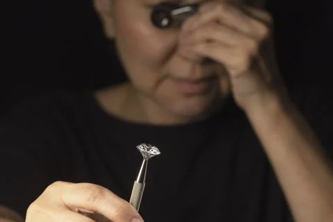 Close up of round cut diamond in hand of asian woman evaluating the quality of Stock Photos