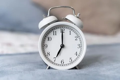 Close-up of a round white alarm clock on a table in the bedroom. Stock Photos