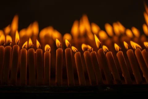 Close up rows of small burning candles capture soft smoke, flickering firel.. Stock Photos