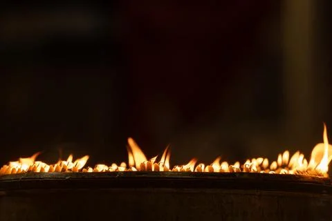 Close up rows of small burning candles capture soft smoke, flickering firel.. Foto stock