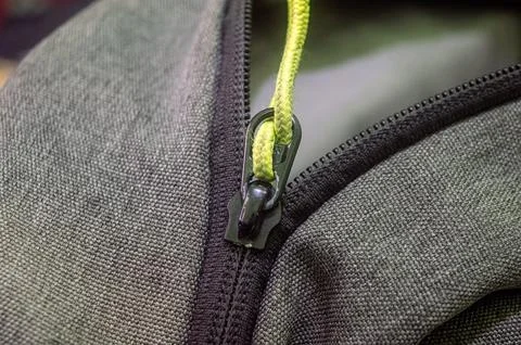 Close up of a rugged backpack zipper with green pull cord on textured fabri.. 스톡 사진