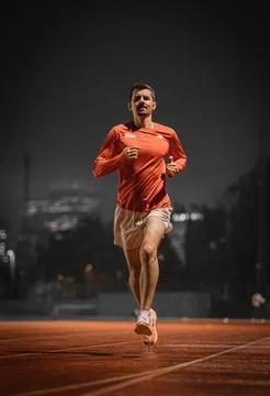 Close up of a runner airborne mid stride on a red track at night 库存照片