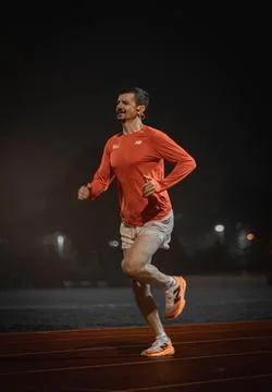 Close up of a runner striding on a red track at night, looking ahead 写真素材