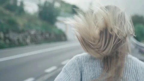 Close-up running after a girl with developing hair on the background of the road Stock Footage 217395346