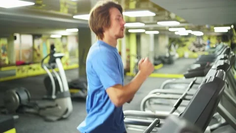 Close-up running redhead guy in a blue t-shirt.treadmill in gym Vidéo 163460778