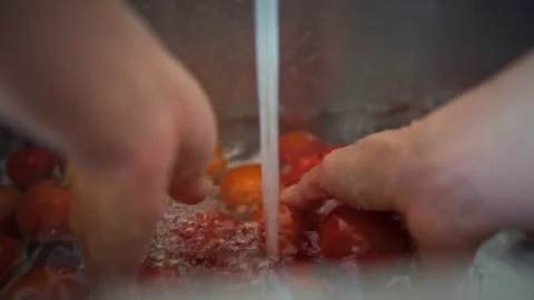 Close-up of running water over fresh organic tomatoes as a womans hands rins Stock Footage 345527537